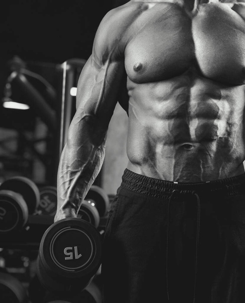 Male bodybuilder holding dumbbell, black and white. - Φωτογραφία, εικόνα