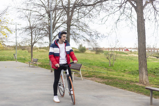 Handsome hipster young man enjoying a bicycle ride and using a smartphone while listening music by headphones - Foto, Imagen