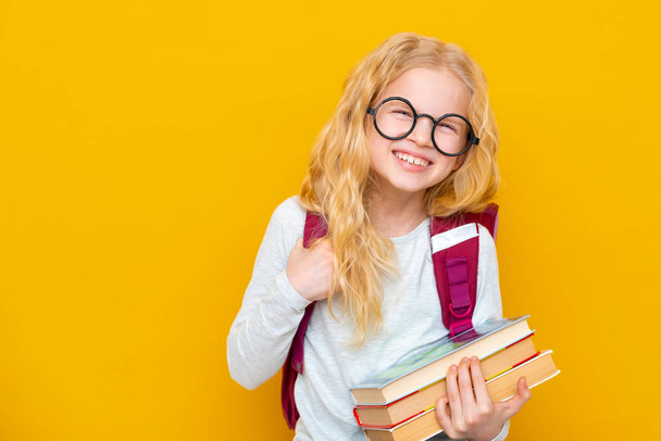 Back to school. Portrait of blonde school girl in round glasses with bag and books. Yellow studio background. Education. smiling at camera. Copyspace - 写真・画像
