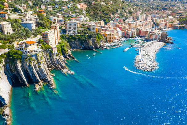 Marina and breakwater where lighthouse is located. Boat sailing to the harbor in ligurian sea, Camogli near Portofino, Italy. Aerial view on traditional Italian colorful houses - 写真・画像