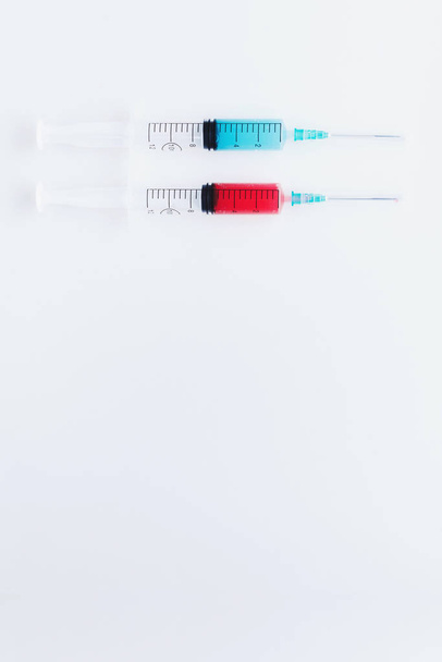 Dos jeringas llenas de líquidos azules y rojos sobre fondo blanco
 - Foto, imagen