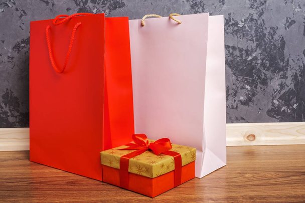 red and pink paper shopping bags and gold gift box on the wooden floor against a concrete wall - Foto, Imagem