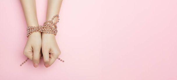 Fashion victim concept flat lay on a pink background. Shopaholics womens hands tied with a rope with beads. Compulsive buying disorder. - Foto, imagen