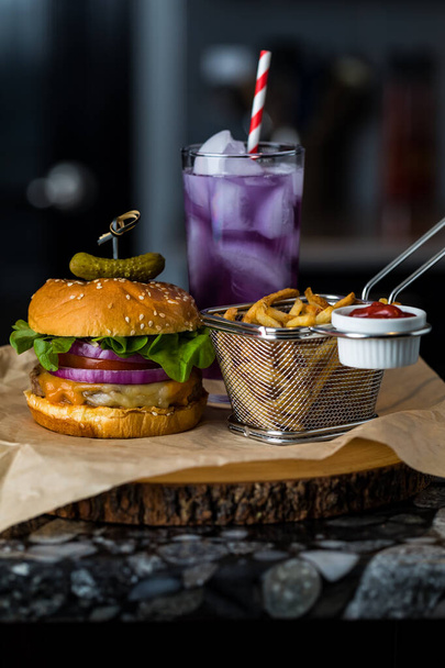 Close up view of a burger and fries with a purple Kombucha mocktail in behind. - Fotoğraf, Görsel