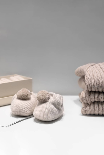 Baby slofjes, truien en sokken gemaakt van natuurlijke beige stoffen liggen op de tafel - Foto, afbeelding