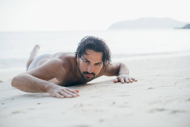Ένας όμορφος άντρας κείτεται στην άμμο δίπλα στον ωκεανό..  - Φωτογραφία, εικόνα