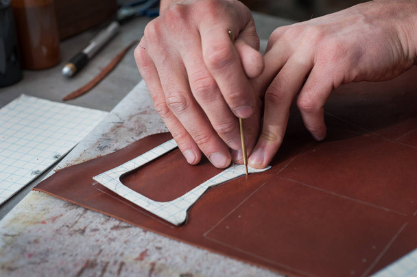 male hands of master cutting with a knife pattern from genuine leather. - Photo, Image