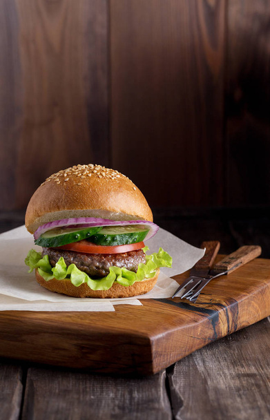Burger on wood board at dark background. - Φωτογραφία, εικόνα