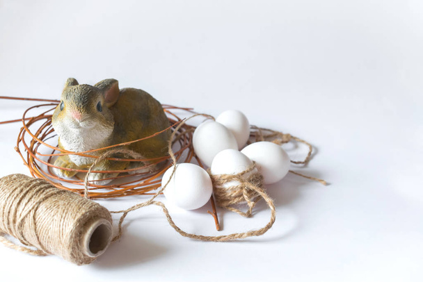 Пасхальные белые яйца и керамическая статуэтка кролика в гнезде на изолированном фоне. Пасхальная композиция
. - Фото, изображение