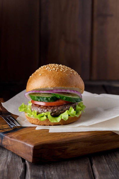 Burger on wood board at dark background. - Фото, изображение
