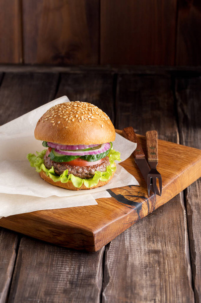 Fresh tasty burger on wooden background close up. Sesame bun with beef, lettuce, tomato, cucumber and onion. Concept of fast food. - Zdjęcie, obraz