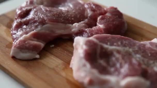 Chef peppering meat on wooden cutting board at professional kitchen. Top view of accompanying uncooked raw steak with pepper. Close up delicious, modern cuisine - Footage, Video