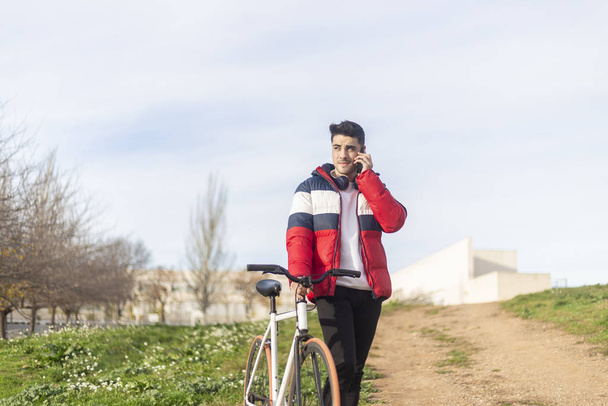 Bel giovane hipster che si gode un giro in bicicletta e utilizza uno smartphone mentre cammina sul parco
 - Foto, immagini