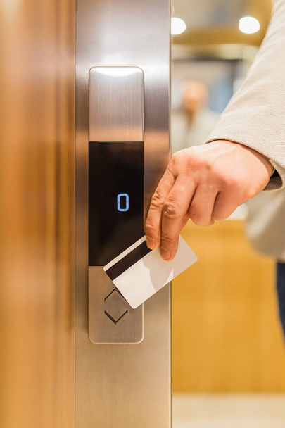 Man holding key card on sensor to open elevator door in modern building or hotel. - Photo, Image