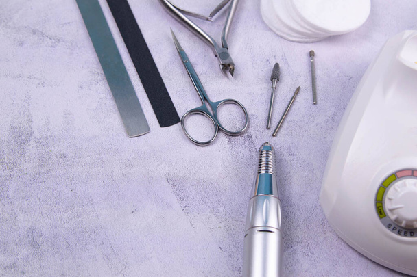 Set of cosmetic tools for manicure and pedicure on a concrete background. Gel polishes, milling cutter, nail files, scissors and tongs. - 写真・画像