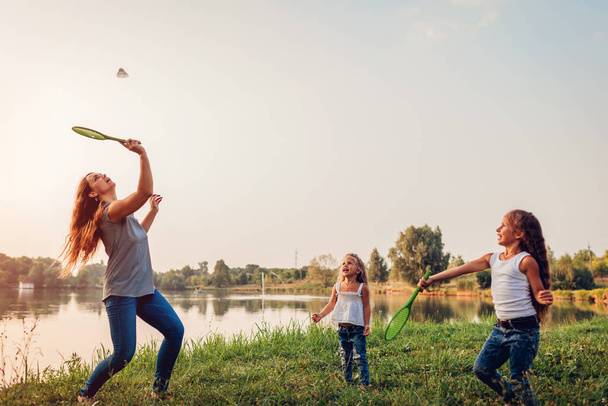 Dzień Matki. Kobieta grająca w badmintona i bawiąca się z córkami w letnim parku. Czas rodzinny - Zdjęcie, obraz