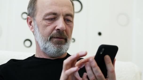 Középkorú, ősz szakállas férfi használja otthon a telefont, közelről. - Felvétel, videó