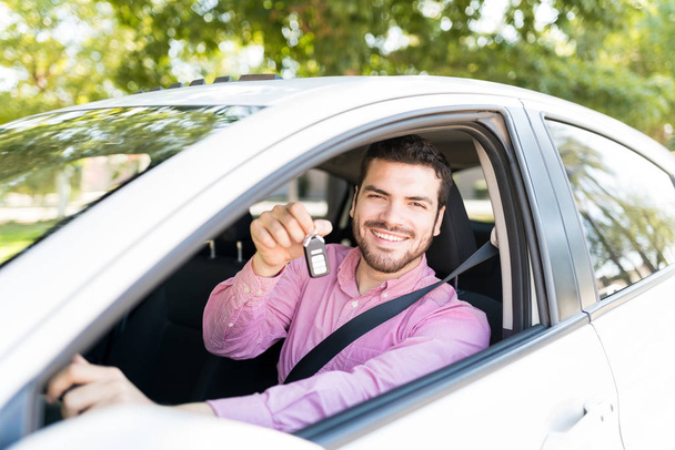 Hombre latino feliz mostrando la llave mientras está sentado en un coche nuevo
 - Foto, Imagen