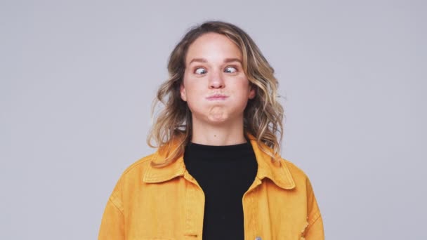 Young woman smiling and laughing as she pulls funny faces into camera against white studio background - shot in slow motion - Video