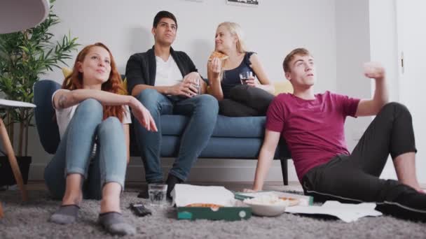 Group of college student friends in shared lounge watching tv and eating pizza together - shot in slow motion - Felvétel, videó
