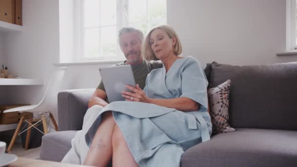 Senior couple sitting on sofa at home using digital tablet together - shot in slow motion - Video, Çekim