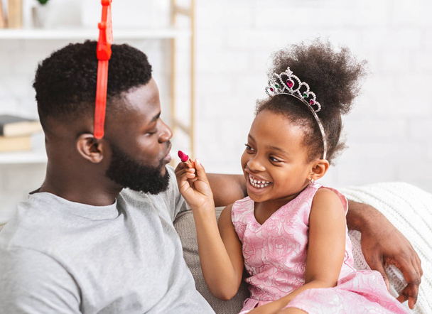 Sonriente afro pequeña hija sosteniendo lápiz labial, jugando con papá
 - Foto, Imagen