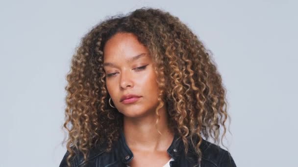 Head and shoulders shot of young woman wearing leather jacket turning to look into camera with serious expression against white studio background - shot in slow motion - Imágenes, Vídeo