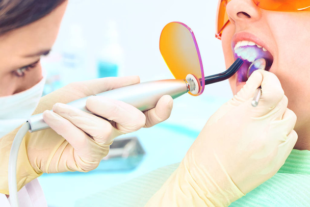 Enfant fille chez le médecin. Dentiste place un remplissage sur une dent avec une lampe de polymérisation dentaire dans la cavité buccale. sur fond clinique
 - Photo, image
