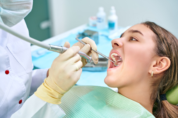 Dívka sedí u zubní židle s otevřenou pusou během orální prohlídky, zatímco doktor. Návštěva zubařské ordinace. Zubní koncept. - Fotografie, Obrázek