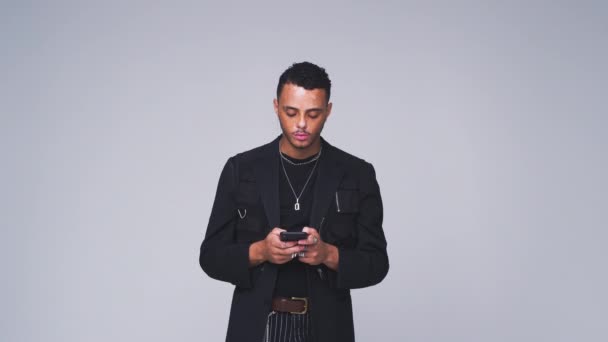 Young man sending text message on mobile phone looks up against white studio background - shot in slow motion - Footage, Video