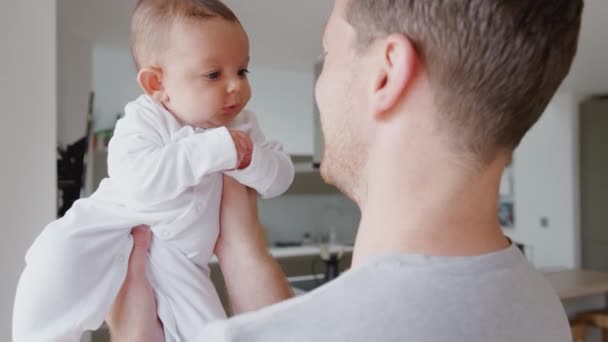 Loving father holding 3 month old baby daughter in kitchen at home playing game by lifting her in the air - shot in slow motion - Materiał filmowy, wideo