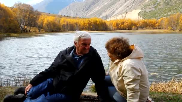 szczęśliwa para starszych, Idąc wzdłuż brzegu jeziora, uśmiechając się, mówić - Materiał filmowy, wideo