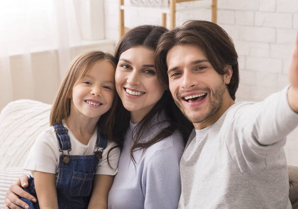 gelukkig familie met schattig dochtertje poseren voor selfie thuis - Foto, afbeelding