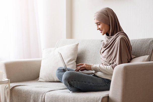 Nuori arabialainen nainen freelancer hijabissa käyttäen kannettavaa tietokonetta kotona
 - Valokuva, kuva