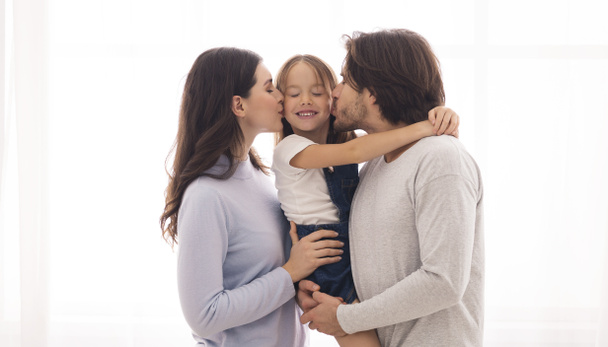Αγαπημένοι γονείς φιλούν την κόρη τους και από τις δύο πλευρές. - Φωτογραφία, εικόνα