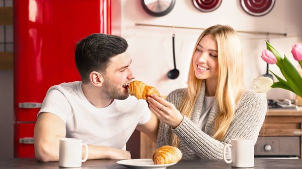 Vrolijke jonge vrouw geven croissant aan haar vriend - Foto, afbeelding