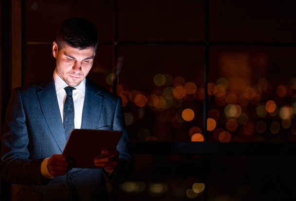 Бизнесмен с использованием цифровых планшетов, стоящих в современном офисе, низкий свет
 - Фото, изображение
