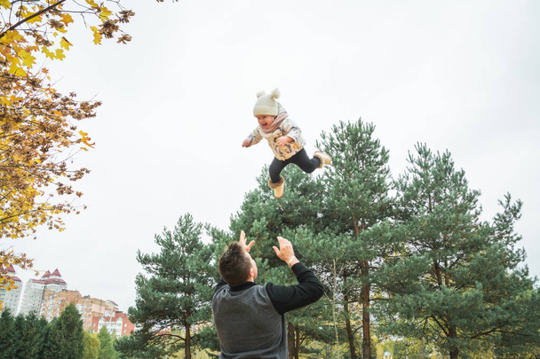 little girl with dad, dad throws baby up in the air, cheerful laughter, emotional child, happiness autumn outdoor - Foto, Imagem