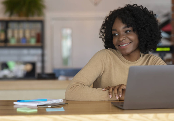 Mujer sonriente sentada en el café. trabajar en línea por ordenador portátil
 - Foto, Imagen