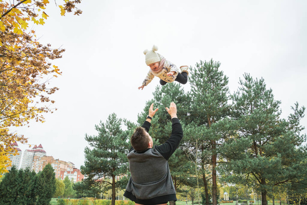 Babasıyla küçük bir kız, babası bebeği havaya fırlatıyor neşeli bir kahkaha, duygusal bir çocuk, mutlu bir sonbahar havası. - Fotoğraf, Görsel