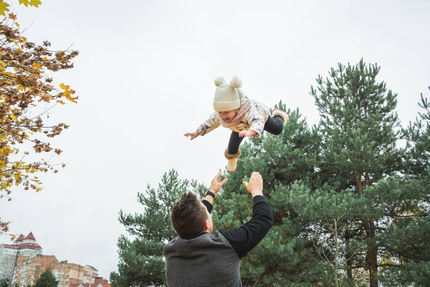 klein meisje met papa, papa gooit baby in de lucht, vrolijk lachen, emotioneel kind, geluk herfst buiten - Foto, afbeelding