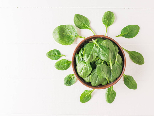 Fresh spinach leaves with a clay bowl on a white wooden table. Food for fitness. The view from the top. - Photo, Image