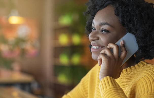 Vista lateral de la joven afro mujer hablando por teléfono inteligente moderno
 - Foto, Imagen