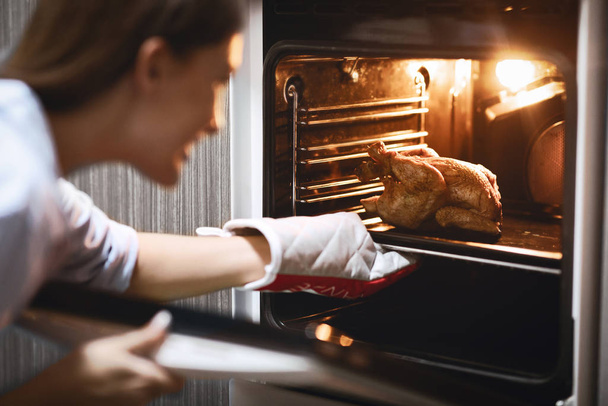 Hausfrau bereitet in Küche gebratenes Hühnchen im Ofen zu - Foto, Bild