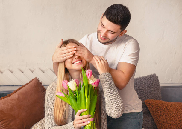 Handsome young man covering eyes of girlfriend and presenting her tulips - Foto, afbeelding