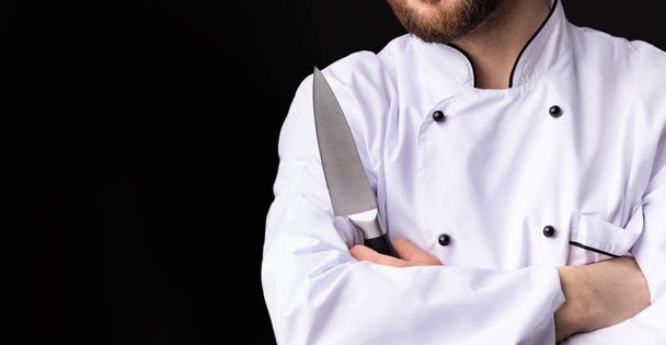 Chef irreconocible sosteniendo cuchillo de pie sobre fondo negro, recortado, Panorama
 - Foto, Imagen