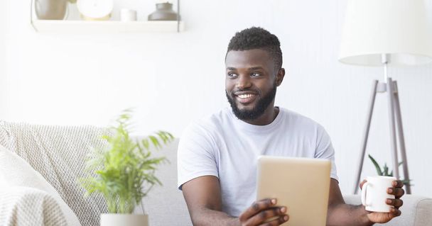 Pozytywny afrykański facet cieszący się poranną kawą i tabletką cyfrową - Zdjęcie, obraz