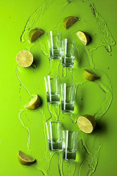 kleine Schnapsgläser mit Limettenscheiben und fließendem Tequila auf einem Gras - Foto, Bild