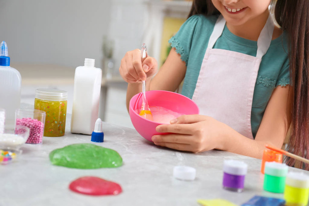 Little girl mixing ingredients with silicone spatula at table in kitchen, closeup. DIY slime toy - Фото, изображение