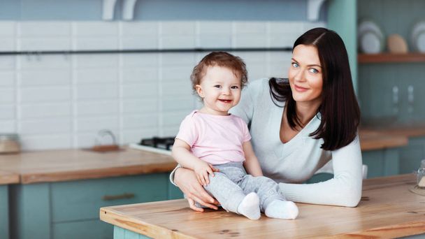 gelukkig weinig baby zitten op de keukentafel met mam en glimlachen - Foto, afbeelding